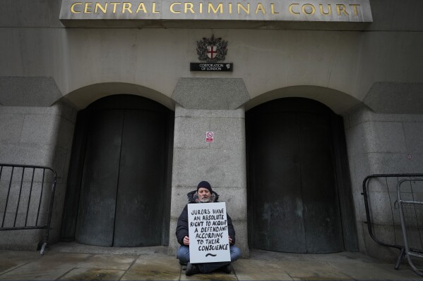 A demonstrator holds a banner outside The Old Bailey, the Central Criminal Court of England and Wales, in London, Monday, Dec. 4, 2023. (AP Photo/Kirsty Wigglesworth)
